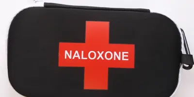 Black pouch with a red cross shape on the front and white embroidery that says naloxone