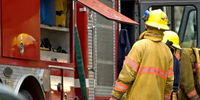 Two firefighters stand at the side of a fire truck with a compartment and door open